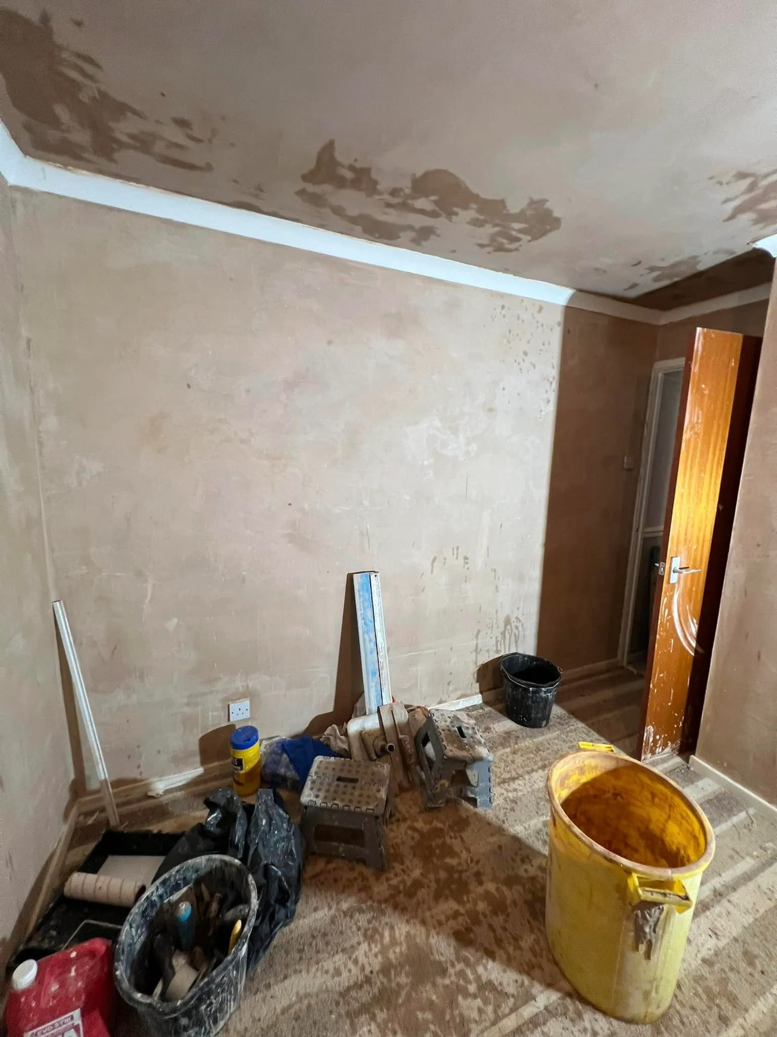 A room with a bucket of paint and tools on the floor.